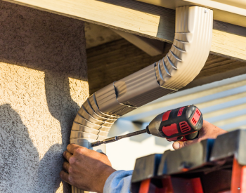 A professional technician replacing seamless gutters on a residential home in Healdsburg, CA, with tools and materials neatly organized.