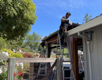 A professional technician replacing gutters on a beautiful home in Sonoma County, CA, with a scenic landscape in the background.